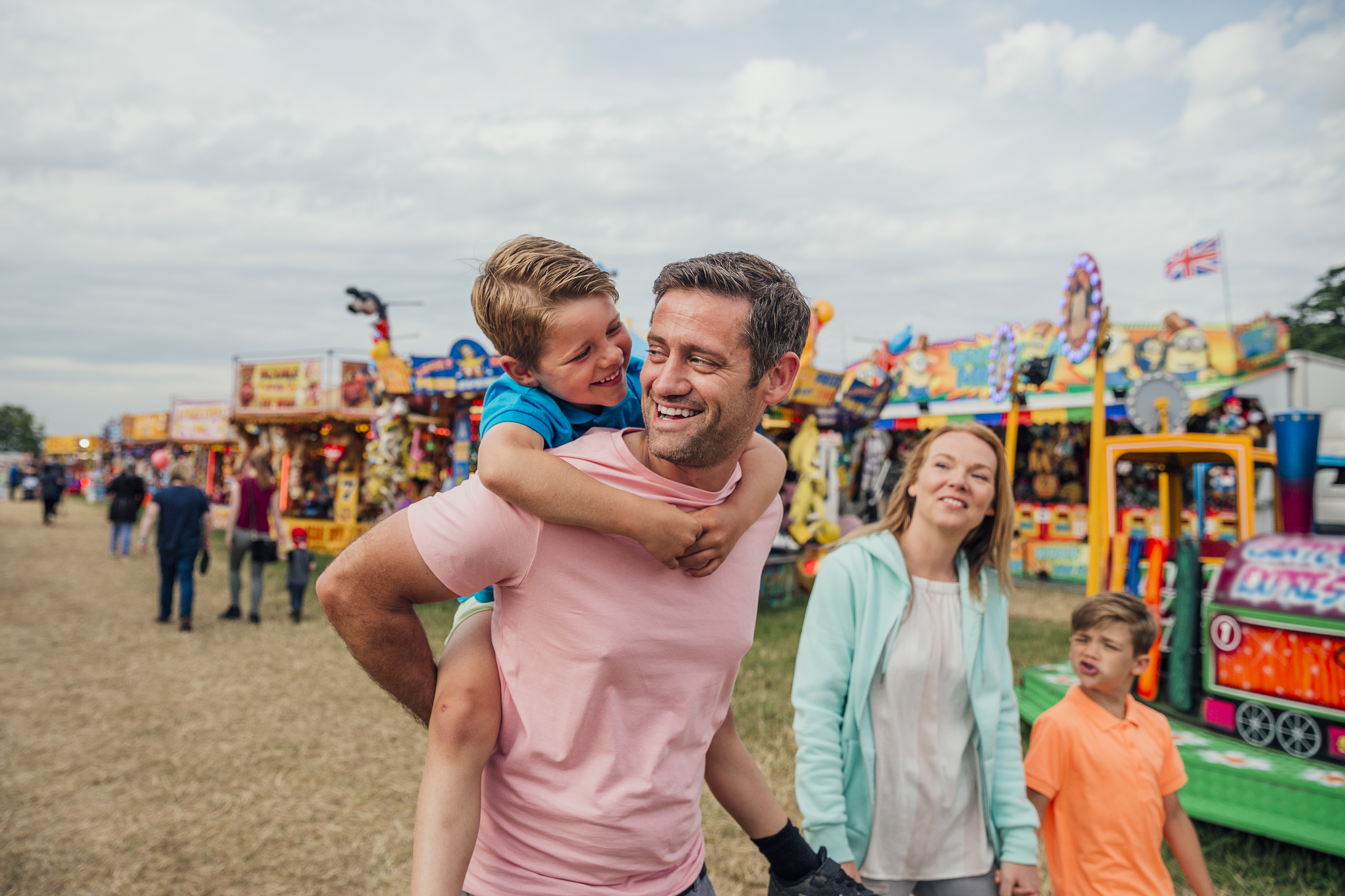 Family Walking Around Carnival With Father Carrying Son on Back