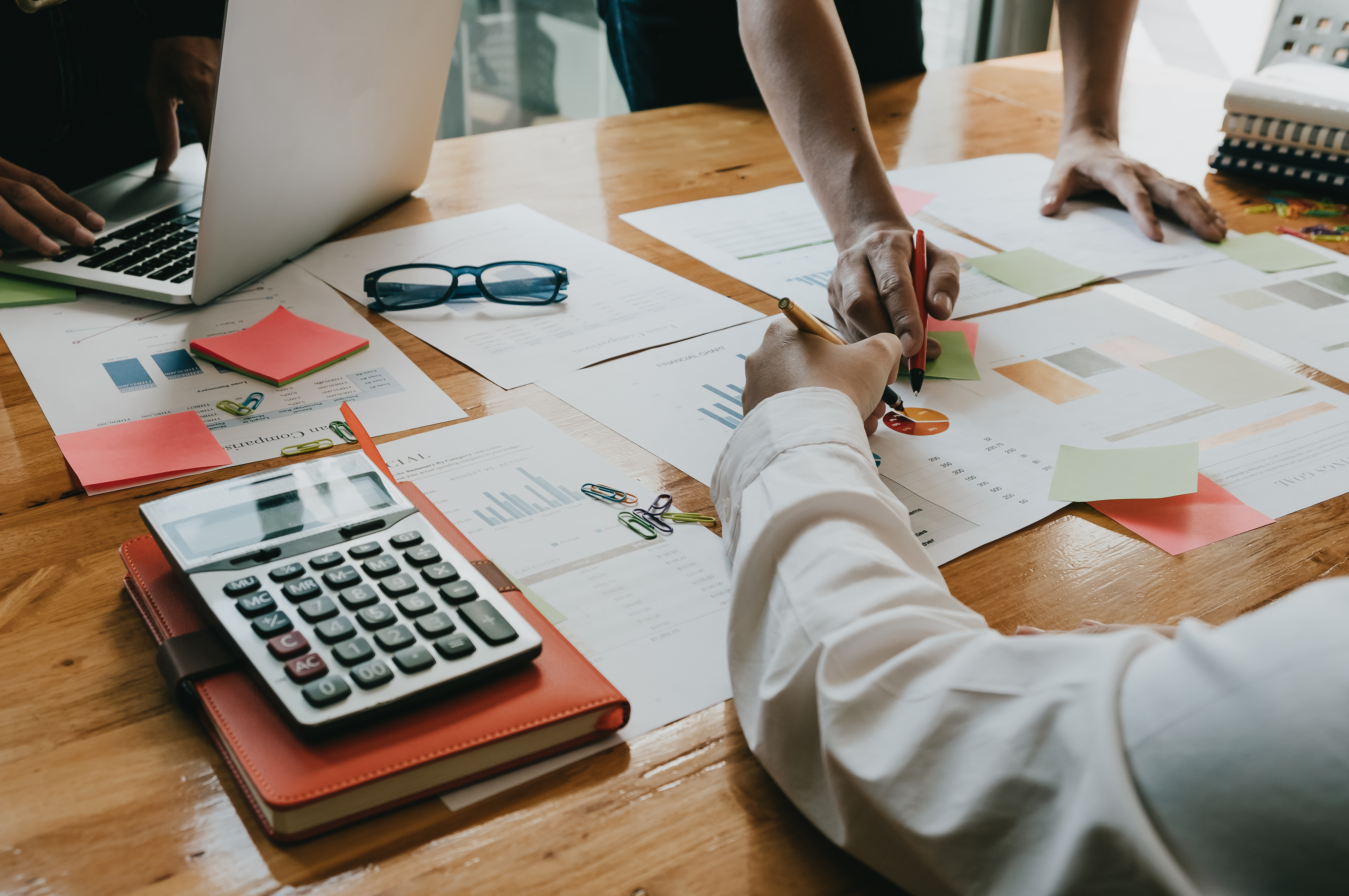 2 sets of hands pointing at a paper with charts while a calculator is out