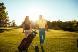 Couple, man and woman, walking on a golf course together at sunset.