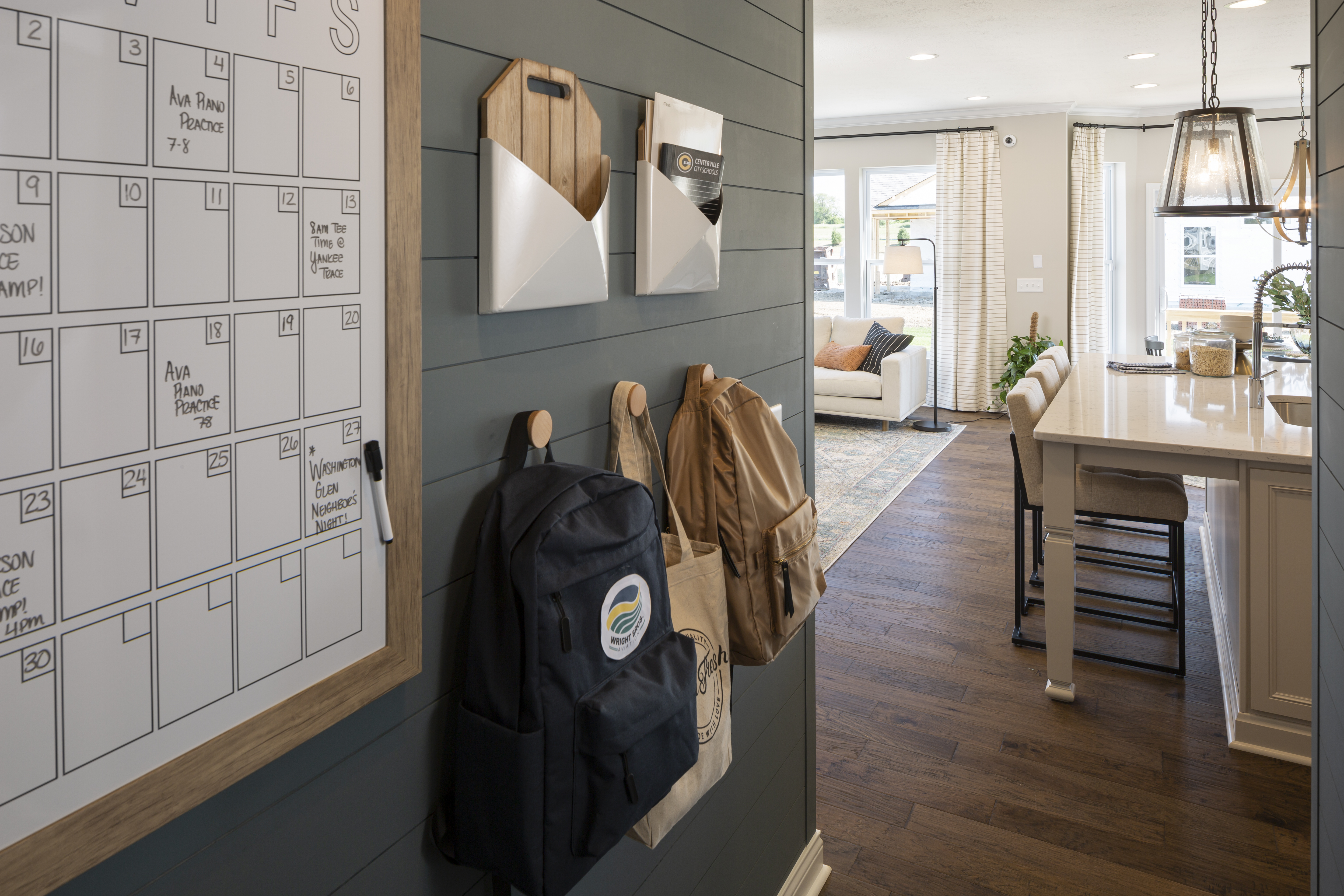 Green wall in a mud room with a calendar and hooks with hanging backpacks