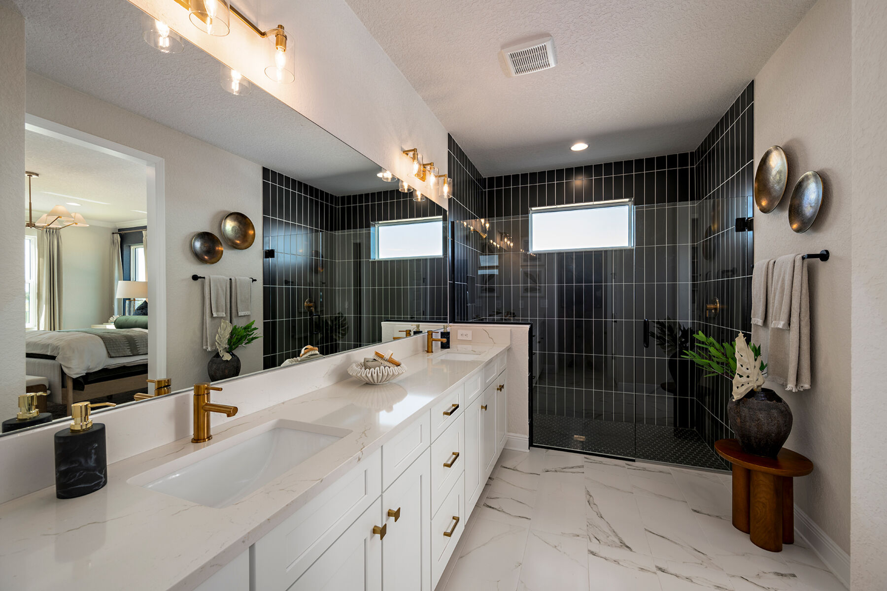 Photo of an owner's bathroom with a double-sink vanity, gold fixtures, white cabinets, quartz counters, and black wall tile