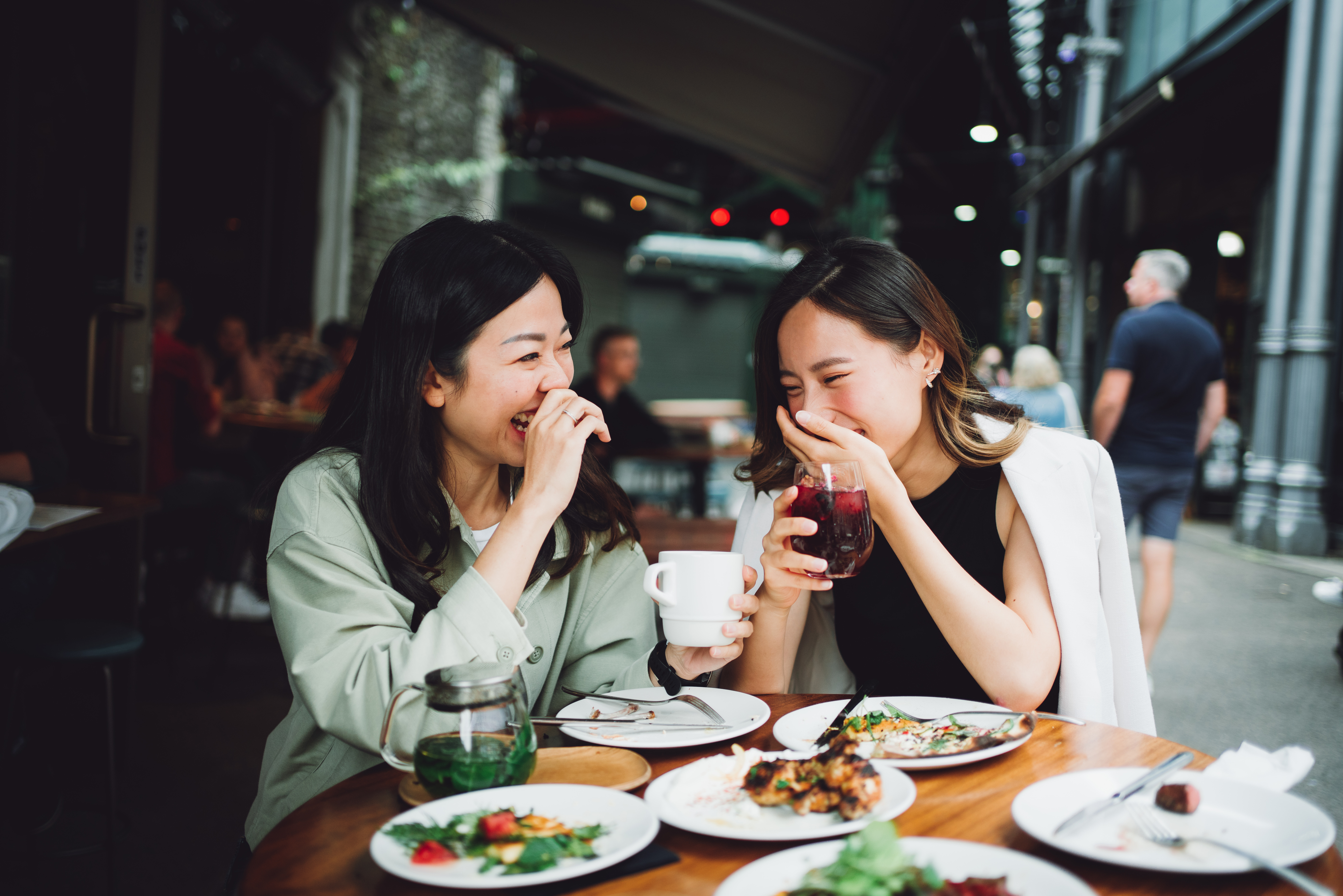 Two Women Laughing Over Wine and Food at Restaurant