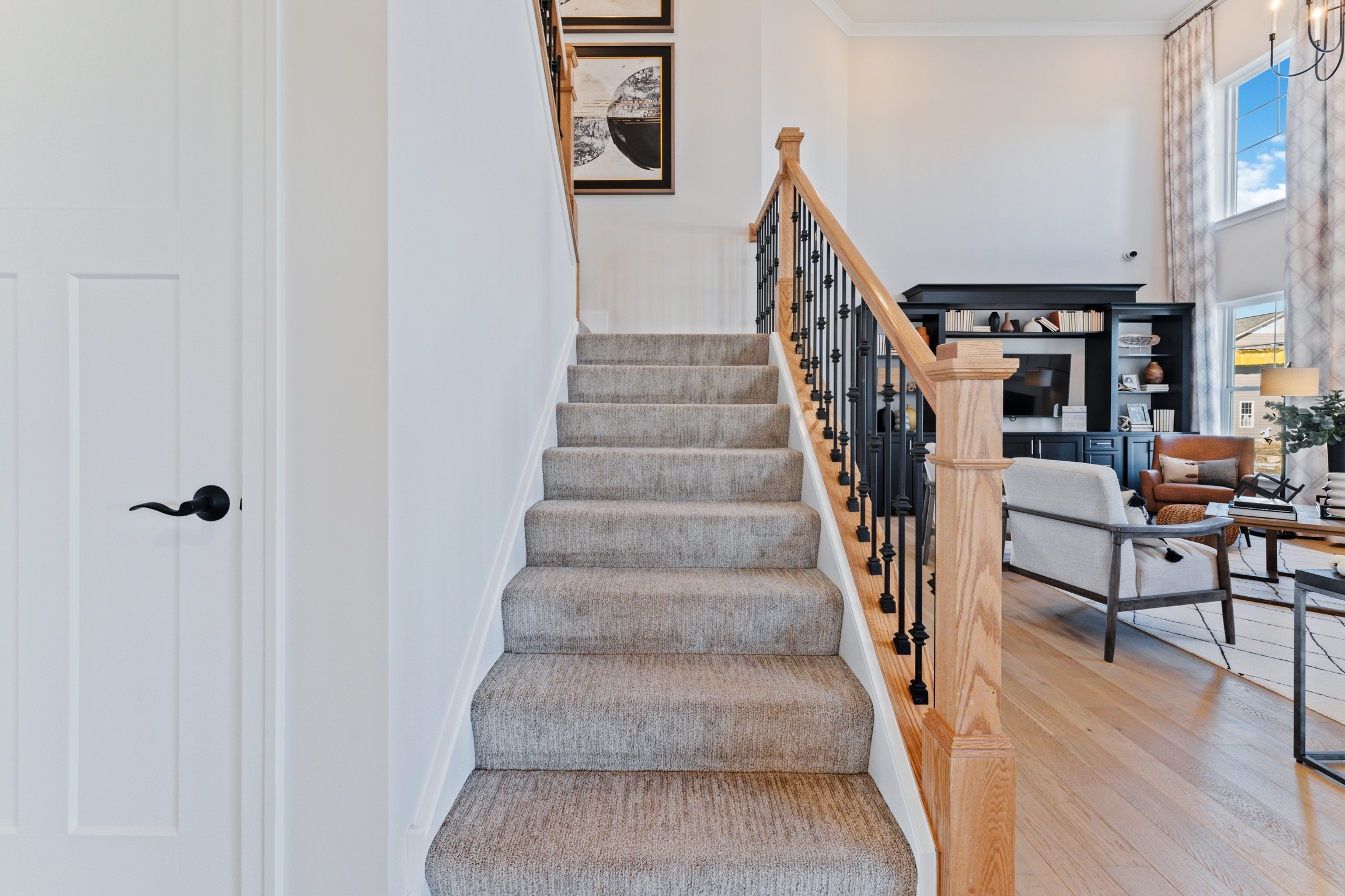 Carpeted staircase in a house heading upstairs with black spindles and a wood banister