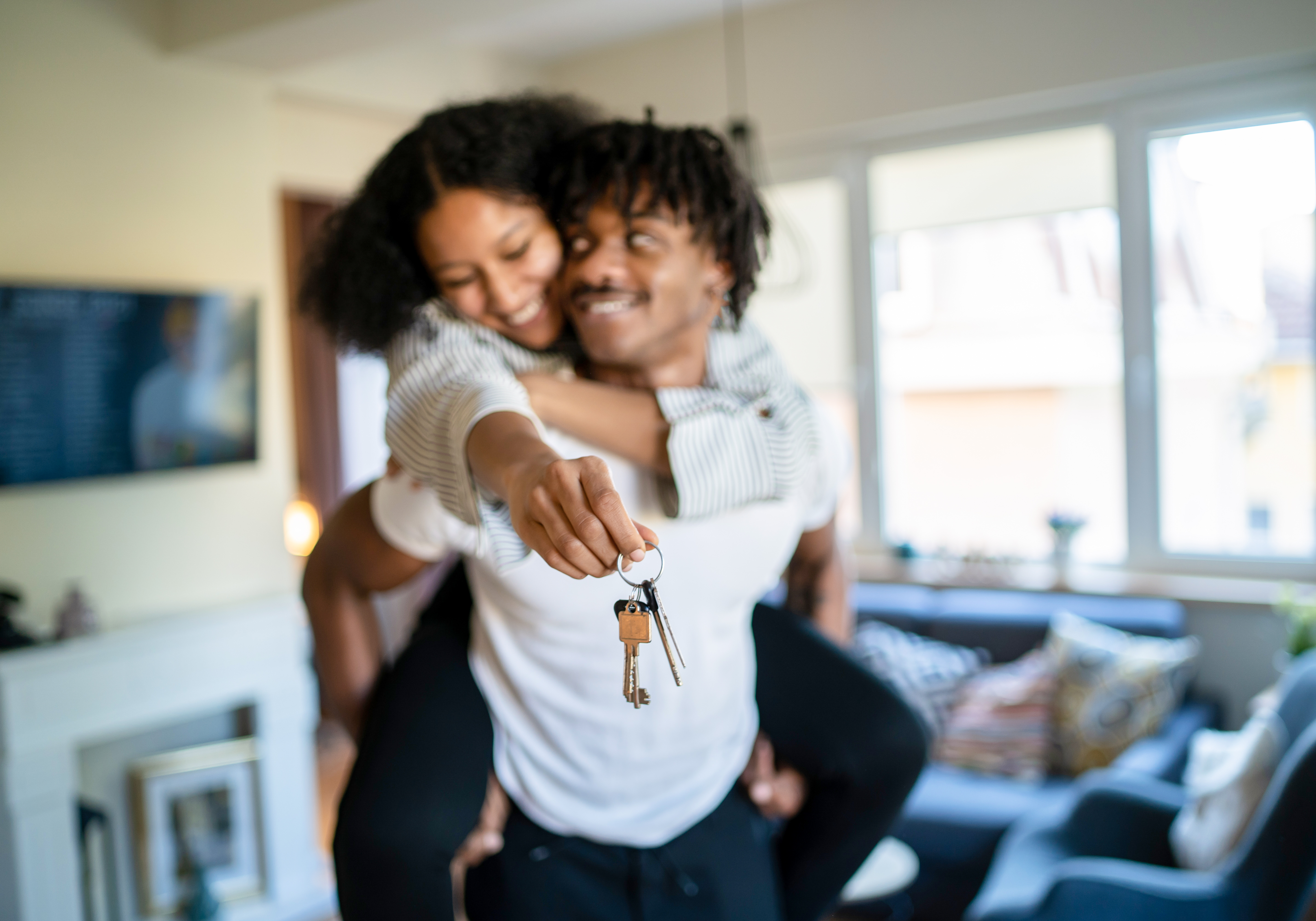 Woman On Man's Back Smiling and Holding Keys To New Home