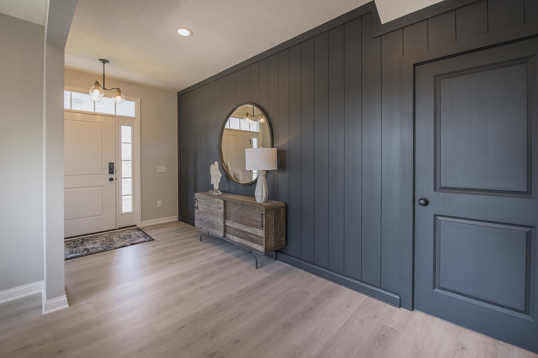 Black shiplap accent wall in a foyer with a console table and mirror